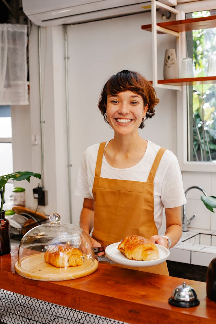 About Charming waitress in apron serving croissant with a smile in a cozy café setting.